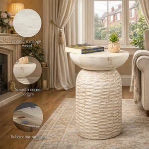 May include: A cream-coloured mango wood side table with a carved, textured base and a smooth, rounded top. The table has smooth corner edges and a rubber bottom grip. A book and a small potted plant sit on top of the table.