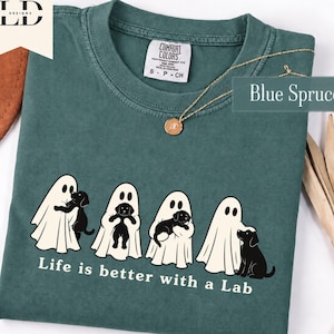 Könnte beinhalten: Ein blau-fichtenfarbenes T-Shirt mit einer Grafik von vier weißen Geistern, die schwarze Labrador-Welpen halten. Der Text unter der Grafik lautet, Life is better with a Lab. Das T-Shirt hat ein Comfort Colors Markenetikett am inneren Halsausschnitt.