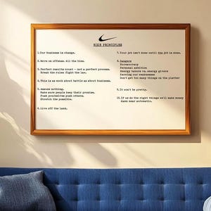 May include: A framed print with the Nike logo and the words "Nike Principles" at the top. The text lists ten principles in a simple, sans-serif font. The frame is brown, and the print hangs above a blue sofa.