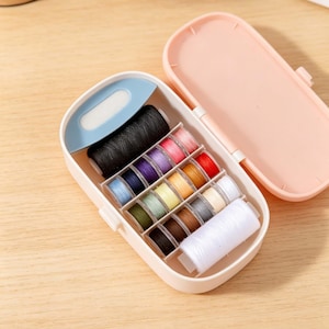 May include: A pink sewing kit with a variety of colorful thread spools. The kit is open, revealing a black spool, a blue thread cutter, and a selection of threads in various colors, including pink, red, and yellow. The kit is designed for easy storage and portability.