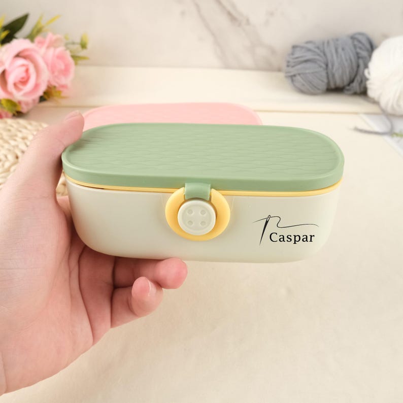 May include: A cream-colored sewing box with a green textured lid and a yellow clasp. The box has the word "Caspar" printed on the side. The box is oval-shaped and appears to be made of plastic.