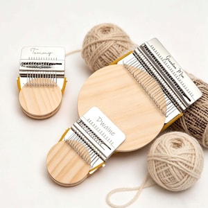 May include: Three wooden weaving looms with metal parts, each engraved with a name: "Tommy", "Dwaine", and "Grandma Mom". Beige yarn balls and skeins are arranged around the looms, indicating a crafting project.