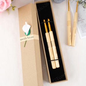 May include: Crochet hooks with wooden handles and gold-coloured metal tips, presented in a brown gift box with the text "specially for you". The hooks are labelled with sizes, and the box has a black interior.