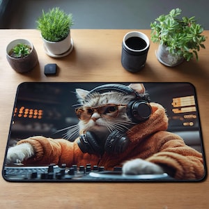Könnte beinhalten: Schwarzes rechteckiges Mauspad mit einer Katze, die Kopfhörer und eine Brille trägt, in einem orangefarbenen Kapuzenpullover gekleidet ist und einen DJ-Mixer bedient. Das Bild hat einen verschwommenen Hintergrund mit Lichtern. Das Mauspad liegt auf einer Holzoberfläche.