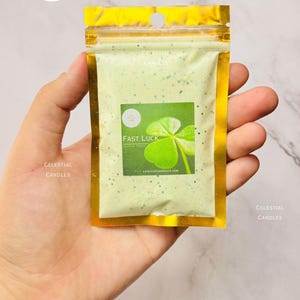May include: A small pouch with gold edging, filled with light green powder. The label displays a green shamrock and the words "Fast Luck". The brand name "Celestial Candles" is printed on the pouch.