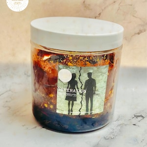 May include: A clear jar with a white lid, filled with a dark, textured substance. A label on the jar reads "SEPERATION" with a graphic of a couple. The jar is on a marble surface.
