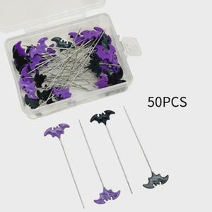 May include: A clear plastic container filled with sewing pins. The pins have silver shafts and bat-shaped heads in black and purple. The text "50PCS" is visible on the right side of the image. Three pins are outside the container.
