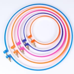 May include: A set of five nested circular embroidery hoops in varying sizes, featuring vibrant plastic frames in blue, orange, pink, purple, and orange. Each hoop includes a metal tension screw mechanism for securing fabric during needlework.