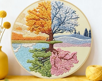 May include: A round embroidery hoop featuring a tree divided into four seasons. The top left shows autumn with orange and yellow leaves, the top right winter with blue and white, the bottom left spring with green, and the bottom right spring with pink blossoms.