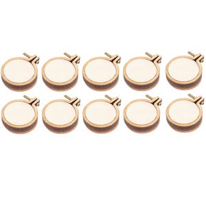 May include: A set of ten small, round embroidery hoops arranged in two rows of five. Each hoop features a dark brown wooden frame with a light-colored fabric center and a metal tightening screw mechanism at the top for securing the material.