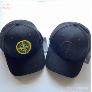 以下が含まれることがあります： 2つの黒い野球帽。1つは黄色と緑の円形エンブレム、もう1つは黒いエンブレムが付いています。どちらの帽子もカーブしたつばと丸いトップが付いています。