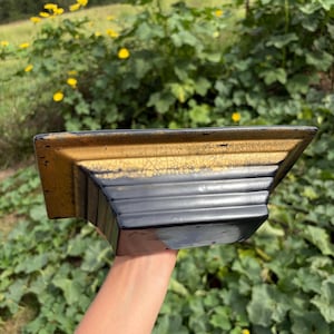 May include: A rectangular ceramic planter featuring a tiered, stepped design. The upper rim displays a distressed gold finish with a visible crackle texture, while the lower body is finished in a solid, smooth, glossy black glaze.