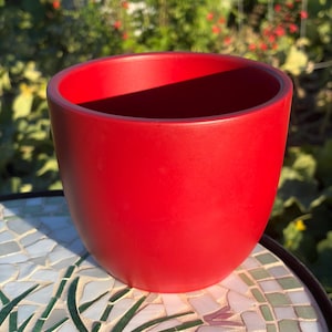 May include: A solid, vibrant red plant pot with a smooth, matte finish and a rounded, cylindrical shape. The pot features a wide, open top and a deep interior, showcasing a clean, minimalist design with no additional patterns or textures.