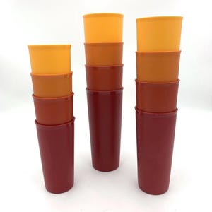 May include: A set of vintage plastic tumblers in shades of orange and red. The cups are stacked in three columns, with the colors transitioning from light orange at the top to deep red at the bottom. The cups are cylindrical with a slight flare at the top.