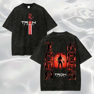May include: A black acid-wash t-shirt featuring a red and white Tron Ares logo on the front. The back displays a large red glowing graphic of a silhouette figure inside a geometric shape, flanked by vertical Tron Ares text in a bold red font.