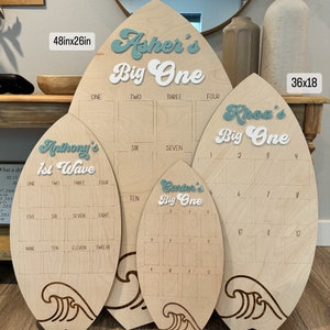 May include: Four wooden surfboard-shaped signs with a wave design at the bottom. The signs are different sizes and feature the names Asher, Khoa, Anthony, and Carter with the text "Big One" and "1st Wave". The signs are numbered 1-12 and are 48x26 inches, 36x18 inches, 30x15 inches, and 24x12 inches.