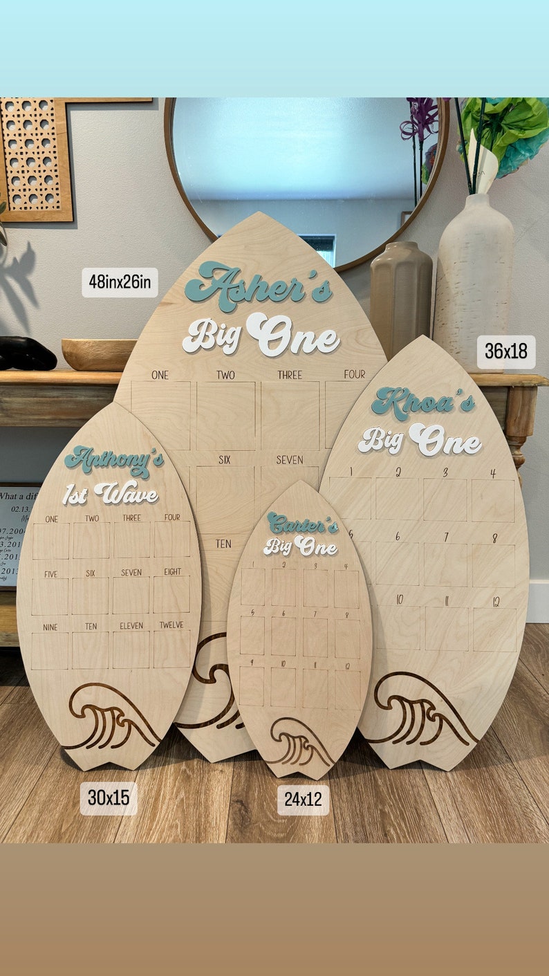 May include: Four wooden surfboard-shaped signs with a wave design at the bottom. The signs are different sizes and feature the names Asher, Khoa, Anthony, and Carter with the text "Big One" and "1st Wave". The signs are numbered 1-12 and are 48x26 inches, 36x18 inches, 30x15 inches, and 24x12 inches.