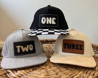May include: Three baseball caps with numbers one, two, and three on them. The caps are black, gray, and beige. The numbers are in white, black, and brown.