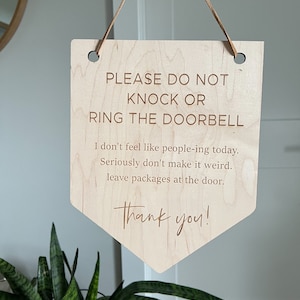 May include: A wooden sign with the text "PLEASE DO NOT KNOCK OR RING THE DOORBELL. I don't feel like people-ing today. Seriously don't make it weird. Leave packages at the door. Thank you!"