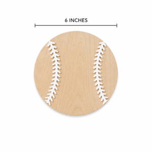 May include: A circular light-colored wooden cutout shaped like a baseball, featuring two white painted curved stitching patterns on the surface. A measurement line above the object indicates a diameter of 6 inches for the wooden baseball.
