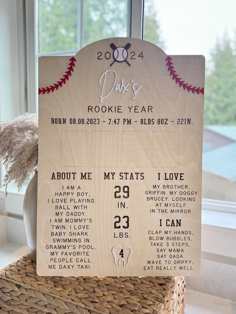 May include: A wooden sign with a baseball theme, celebrating a baby's first year. The sign includes the baby's name, Dax, and details about their birth date, weight, and length. It also includes information about the baby's milestones, such as their height, weight, and number of teeth.
