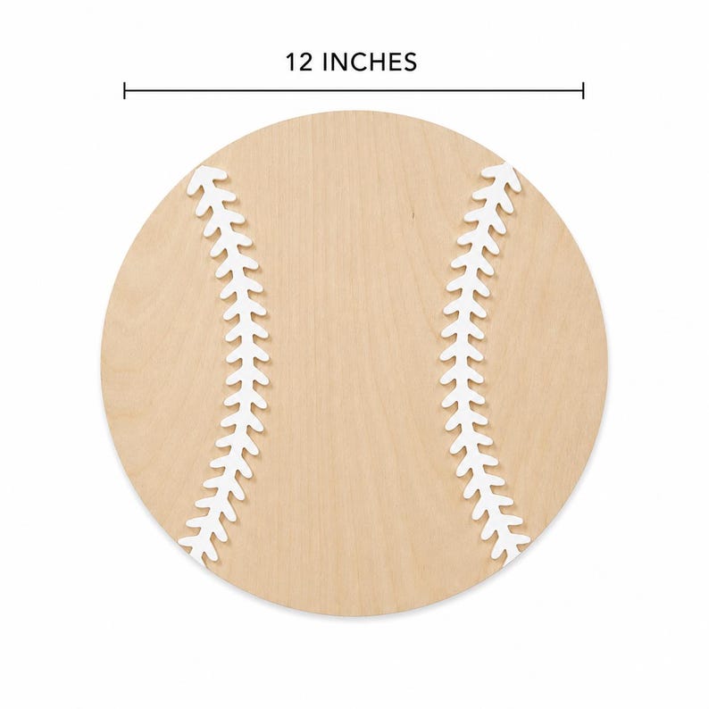 May include: A circular wooden cutout shaped like a baseball, featuring a light tan wood grain finish and two curved white painted lines representing the stitching. The object is labeled with a measurement line indicating a diameter of 12 inches.