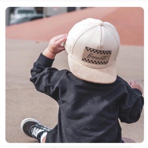 May include: A cream colored suede baseball cap with a brown checkered patch that says "Bennett" in black script.