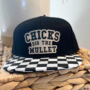 May include: Black and white checkered baseball cap with a black crown and a white patch that says "CHICKS DIG THE MULLET".
