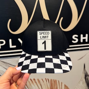 May include: Black and white checkered baseball cap with a black patch that says "Speed Limit 1" on it.