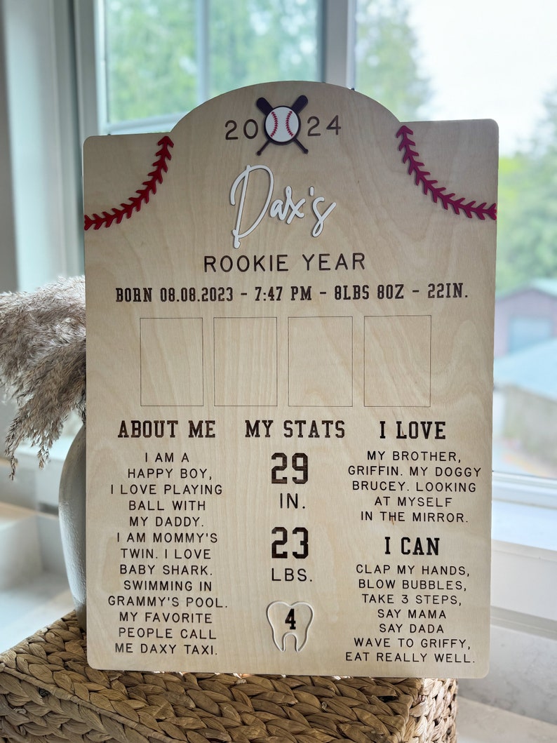 May include: A wooden sign with a baseball theme, celebrating a baby's first year. The sign features the baby's name, "Dax's", and details about their birth, including the date, time, weight, and length. It also includes a section about the baby's personality, stats, and favorite things.