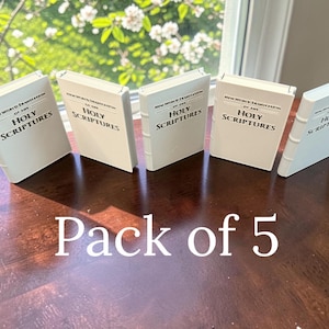 May include: A set of five miniature white books standing upright. Each book features a black printed title that reads New World Translation of the Holy Scriptures. The books have a smooth, matte finish with raised spine details and are arranged in a row.