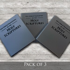 May include: Three books with gray covers are displayed on a light wood-grain surface. The text "NEW WORLD TRANSLATION OF THE HOLY SCRIPTURES" is printed on the covers. The phrase "PACK OF 3" is at the bottom.