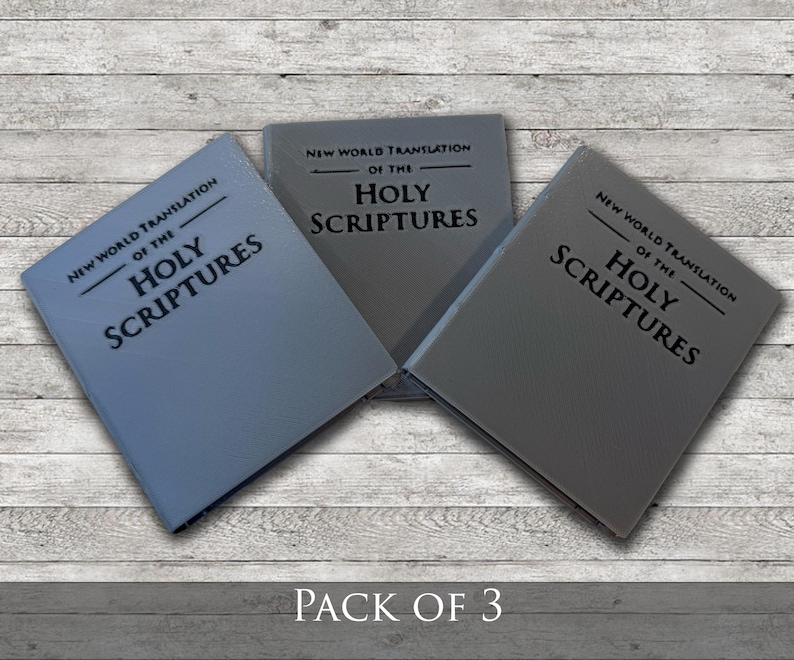 May include: Three books with gray covers are displayed on a light wood-grain surface. The text "NEW WORLD TRANSLATION OF THE HOLY SCRIPTURES" is printed on the covers. The phrase "PACK OF 3" is at the bottom.