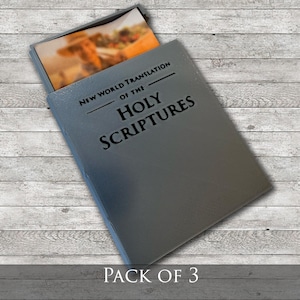 Puede incluir: Un libro gris con el texto "NEW WORLD TRANSLATION OF THE HOLY SCRIPTURES" está parcialmente abierto, revelando una imagen colorida. Las palabras "PACK OF 3" están impresas en la parte inferior de la imagen.