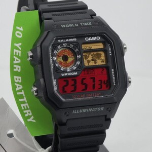 May include: Black Casio digital watch with a rectangular face. The watch displays the time in red digits and features a world map and various functions. The watch has the text "WORLD TIME", "CASIO", and "10 YEAR BATTERY".