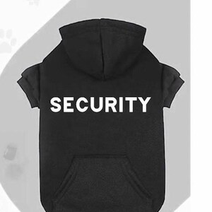 May include: Black dog hoodie with the word "SECURITY" printed in white block letters across the chest. The hoodie has a hood and a front pocket. The sleeves are short and rolled up.