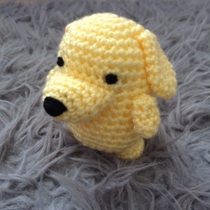 Könnte beinhalten: Ein gehäkeltes gelbes Hundespielzeug mit schwarzen Augen und einer schwarzen Nase.