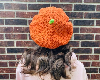 May include: A crocheted orange beret with a green pom-pom on top.