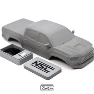 Può includere: Una carrozzeria di camioncino grigia non verniciata con un piccolo contenitore rettangolare grigio separato contenente componenti neri e argentati. È inclusa una targa rettangolare grigia con il testo nero NSL, abbinata al logo NSL sottostante.