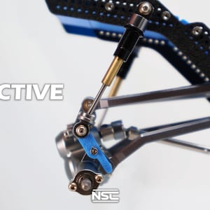 Pu&ograve; includere: Primo piano di un componente meccanico con la scritta "ACTIVE" in bianco. Il componente presenta parti nere, blu e argentate, tra cui un ammortizzatore e vari collegamenti. Il design suggerisce precisione e ingegneria.