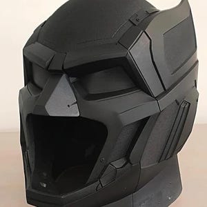 May include: A black, futuristic-looking helmet with a textured surface. The helmet has angular features, including a prominent visor and cheek guards. The design suggests a sci-fi or cosplay theme.