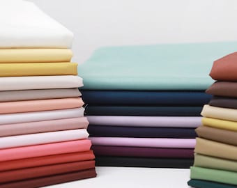 May include: A stack of fabric swatches in various colors, including white, yellow, beige, pink, red, brown, green, blue, and purple. The fabric swatches are arranged in a neat pile, showcasing the different colors and textures.
