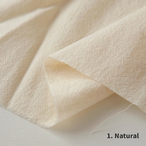 May include: Close-up of a natural-coloured fabric with a textured surface. The fabric is folded over itself, showing the soft, natural texture.