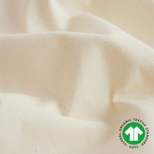 Może przedstawiać: Zbliżenie na kremowy materiał o subtelnej fakturze. Materiał posiada zieloną etykietę certyfikatu Global Organic Textile Standard (GOTS).