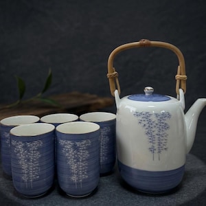 May include: A ceramic tea set featuring a white teapot with a blue lid and bamboo handle, and five matching blue cups. The teapot and cups are decorated with a bamboo design.