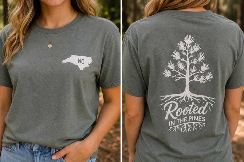 K&ouml;nnte beinhalten: Ein schiefergr&uuml;nes Kurzarm-T-Shirt mit einer wei&szlig;en Grafik des Umrisses von North Carolina und den Buchstaben NC auf der Brust sowie einer gro&szlig;en wei&szlig;en Kieferngrafik mit Wurzeln und dem Text Rooted IN THE PINES auf der R&uuml;ckseite.