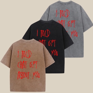 May include: Three short-sleeved t-shirts in brown, black, and gray. Each shirt has the red text "I TOLD CHAT GPT ABOUT YOU" or "I TOLD WHAT GPT YOU" printed on the back. The shirts have a vintage, washed appearance.