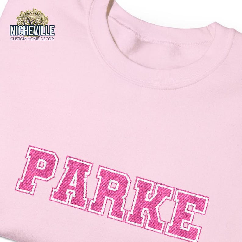 Close-up detail of pink varsity PARKE embroidery style text on light pink sweatshirt showing textured stitch appearance and premium custom personalization, Nicheville custom embroi
