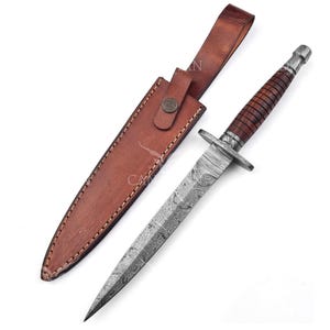 Puede incluir: Una daga de acero de Damasco con un mango de cuero marrón y una funda a juego. La hoja tiene un patrón detallado, y el mango está envuelto en cuero marrón oscuro. La funda tiene un lazo para cinturón y un cierre a presión.