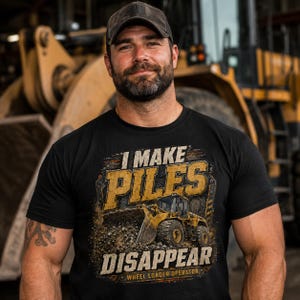 May include: Black t-shirt with the text "I MAKE PILES DISAPPEAR" and a graphic of a yellow wheel loader. The shirt also says "WHEEL LOADER OPERATOR" at the bottom. The person in the image is wearing a dark baseball cap.